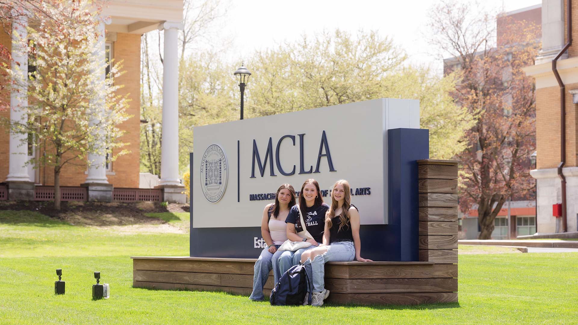 MCLA campus sign with students sitting near it